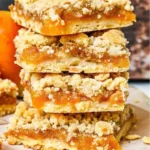 Gluten-free and dairy-free Apricot Crumble Bars cut into squares on a white serving plate, showing layers of golden crumble and vibrant orange apricot filling