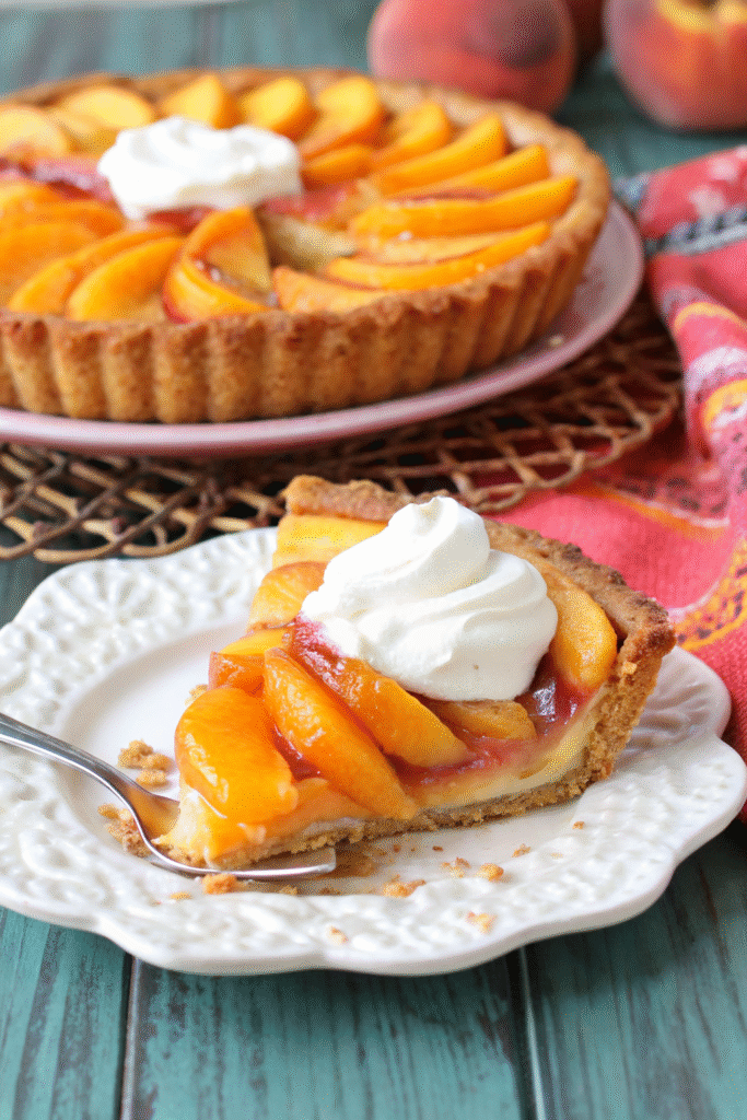 Golden brown peach tart with overlapping peach slices arranged in concentric circles, topped with crumbly butter mixture, served on white plate with dollop of whipped cream