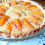 Golden-brown peaches and cream pie with custard filling and cinnamon on top, served in a flaky pie crust