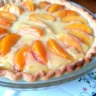 Golden-brown peaches and cream pie with custard filling and cinnamon on top, served in a flaky pie crust