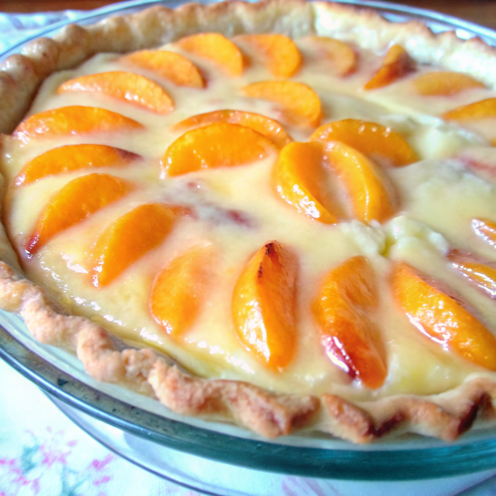 Golden-brown peaches and cream pie with custard filling and cinnamon on top, served in a flaky pie crust