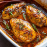 Golden baked honey dijon chicken pieces in a white baking dish with fresh rosemary sprigs and glossy honey mustard glaze