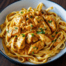 Close-up photo of creamy cowboy butter chicken linguine in a white bowl, showing golden-brown chicken pieces coated in herb-flecked butter sauce tossed with linguine pasta, garnished with fresh parsley and grated Parmesan cheese