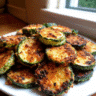 Golden brown crispy parmesan zucchini rounds on white plate with marinara sauce for dipping" Caption: "Perfectly crispy Parmesan zucchini that's golden, crunchy, and absolutely irresistible