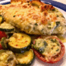 Golden-brown breaded chicken breasts baked with tender zucchini rounds, sliced tomatoes, and melted mozzarella cheese in a rectangular baking dish, garnished with fresh green basil leaves