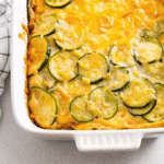 Golden brown keto zucchini casserole in a white baking dish, topped with melted Colby-Jack cheese and showing layers of tender zucchini in a creamy sauce