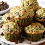Golden brown chocolate chip zucchini muffins arranged on a white cooling rack with mini chocolate chips scattered around