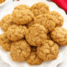 Golden brown soft pumpkin oatmeal cookies arranged on a white plate with scattered oats and a small pumpkin in the background