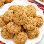 Golden brown soft pumpkin oatmeal cookies arranged on a white plate with scattered oats and a small pumpkin in the background