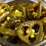 Golden candied jalapenos slices in glass jars with sweet syrup, perfect for adding sweet heat to any meal