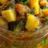 Vibrant orange and red spicy pineapple jalapeño chutney in a glass jar, showing chunky texture with visible diced pineapple pieces and flecks of jalapeño and spices.