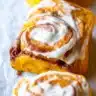Freshly baked pumpkin cinnamon rolls with maple cream cheese icing in a baking pan, golden brown and perfectly swirled