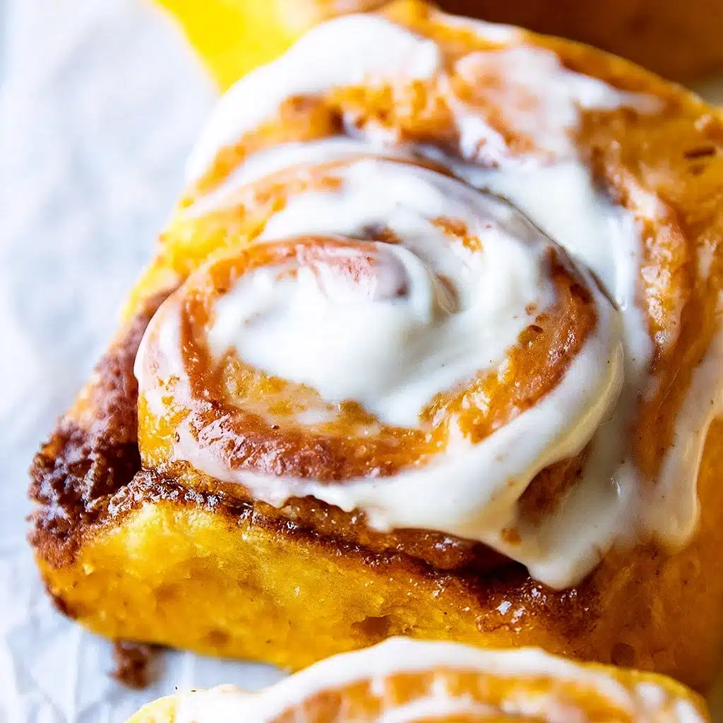 Freshly baked pumpkin cinnamon rolls with maple cream cheese icing in a baking pan, golden brown and perfectly swirled