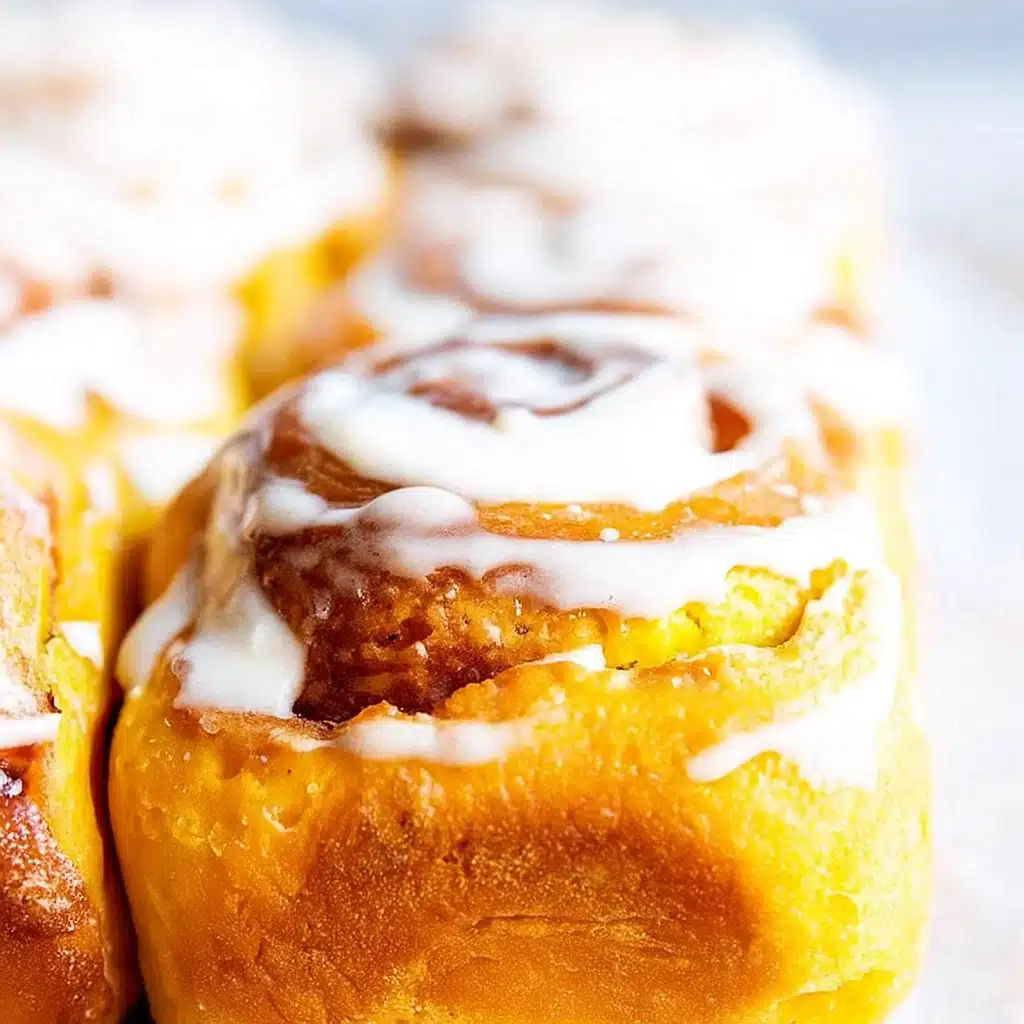 Freshly baked pumpkin cinnamon rolls with maple cream cheese icing in a baking pan, golden brown and perfectly swirled