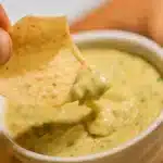 Creamy golden Hatch chile queso in a serving bowl surrounded by tortilla chips, garnished with fresh cilantro and diced green chiles
