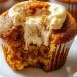 Golden pumpkin cream cheese swirl muffins with beautiful marbled cream cheese ribbons on a rustic wooden board, surrounded by fall leaves and cinnamon sticks