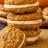 Golden Pumpkin Oatmeal Cream Pies with white cream filling, stacked on a wood board.