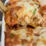 A slice of golden-brown zucchini lasagna on a white plate, showing layers of tender zucchini, creamy ricotta, melted mozzarella, and rich marinara sauce