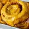 Homemade pumpkin pie cinnamon rolls with cream cheese frosting, showing swirled layers of spiced pumpkin filling