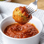 Golden brown zucchini garlic bites arranged on a white platter with fresh basil garnish and marinara dipping sauce in a small bowl