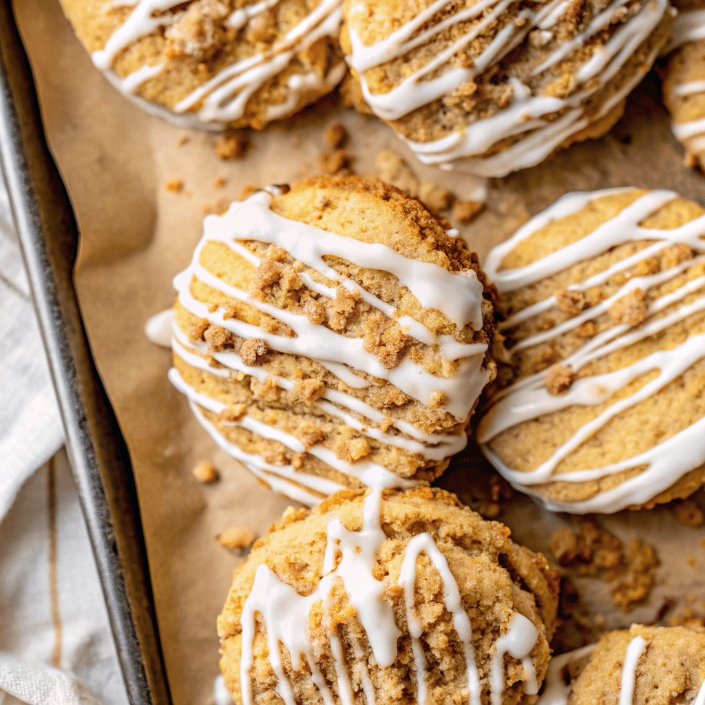 Golden brown pumpkin Coffee Cake cookies topped with buttery crumb topping and drizzled with white glaze, arranged on a cooling rack with fall leaves in the background.