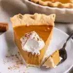 Golden brown pumpkin pie with flaky crust, garnished with sugared cranberries and whipped cream, served on a rustic wooden table with fall decorations