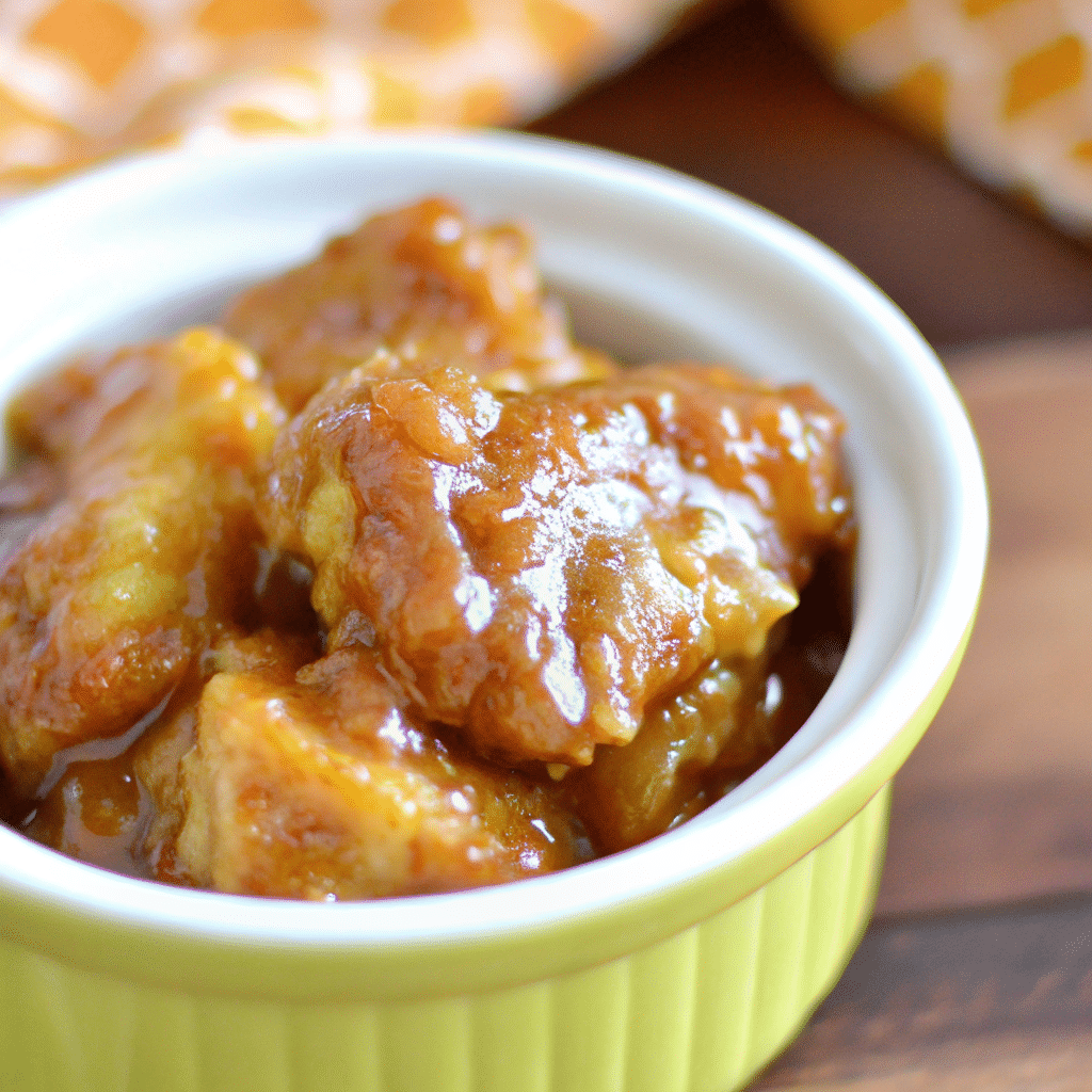 Golden-brown pumpkin bread pudding in a baking dish, topped with toasted pecans and drizzled with caramel sauce, with a spoon taking a bite showing the custardy interior.