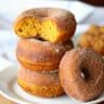 Mini pumpkin spice donuts with cinnamon sugar coating on a wooden board with coffee cups and fall leaves.