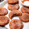 Stack of golden-brown chewy vegan pumpkin spice cookies with cinnamon-sugar coating on a rustic wooden board, surrounded by autumn leaves and pumpkin spices