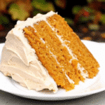 A slice of moist pumpkin spice cake on a white plate with a fork, showing the tender orange-colored crumb studded with raisins.