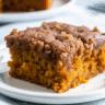 Golden pumpkin coffee cake with crumbly streusel topping and white glaze drizzle on parchment paper