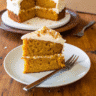 A square piece of moist pumpkin spice Latte cake topped with creamy espresso buttercream frosting on a white plate, with fall leaves and coffee beans scattered nearby