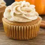 Pumpkin cupcakes topped with cinnamon cream cheese frosting, arranged on a cooling rack with fall-themed decor.