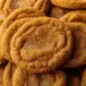 Stack of golden brown chewy maple pumpkin cookies with crackled tops, rolled in cinnamon sugar, displayed on rustic wooden board with fall leaves