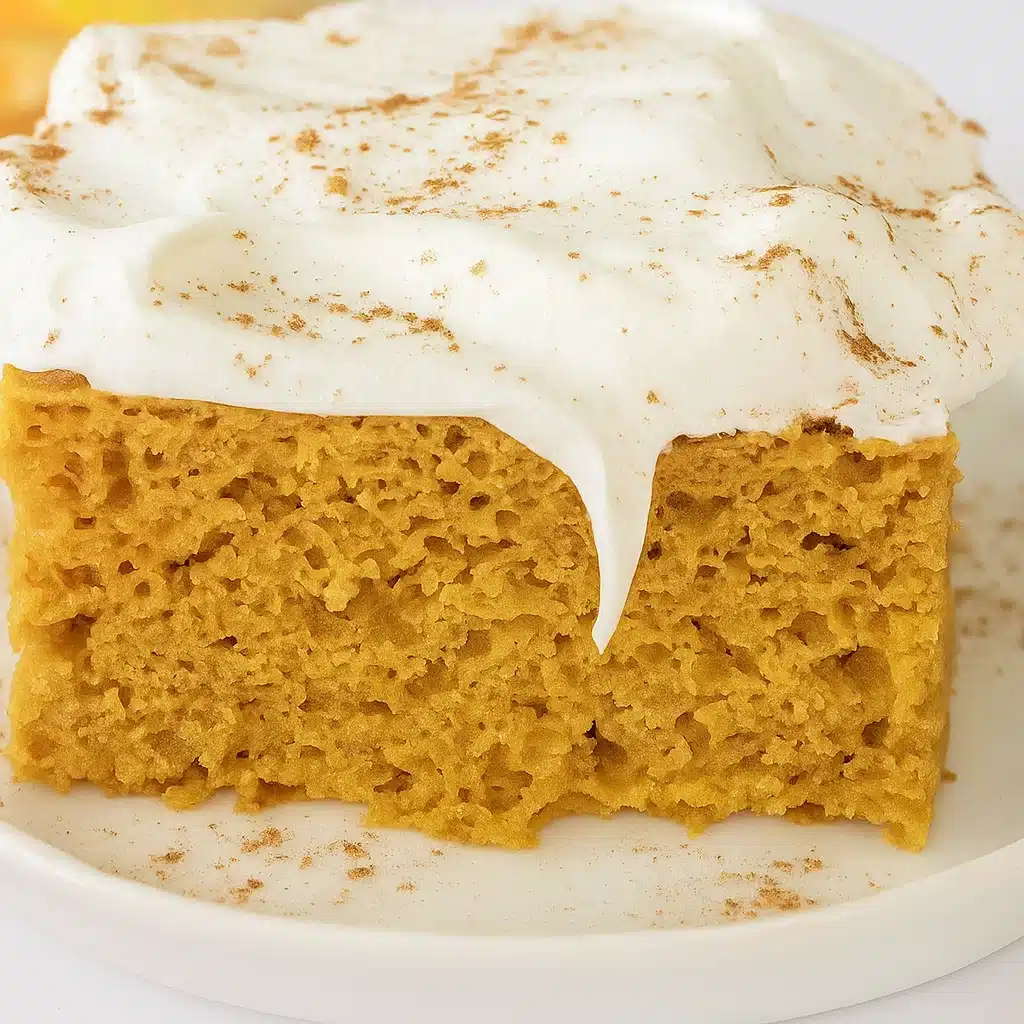 A slice of moist pumpkin spice cake on a white plate with a fork, showing the tender orange-colored crumb studded with raisins.