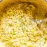 A rustic bowl of creamy one pot delicata squash orzo garnished with fresh thyme and grated Parmesan cheese, photographed from above on a wooden table