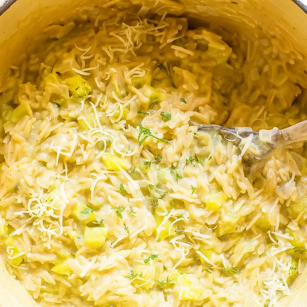 A rustic bowl of creamy one pot delicata squash orzo garnished with fresh thyme and grated Parmesan cheese, photographed from above on a wooden table