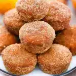 Golden-brown donut pumpkin muffins coated in cinnamon sugar, arranged on a rustic wooden board with fall leaves in the background