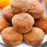 Golden-brown donut pumpkin muffins coated in cinnamon sugar, arranged on a rustic wooden board with fall leaves in the background