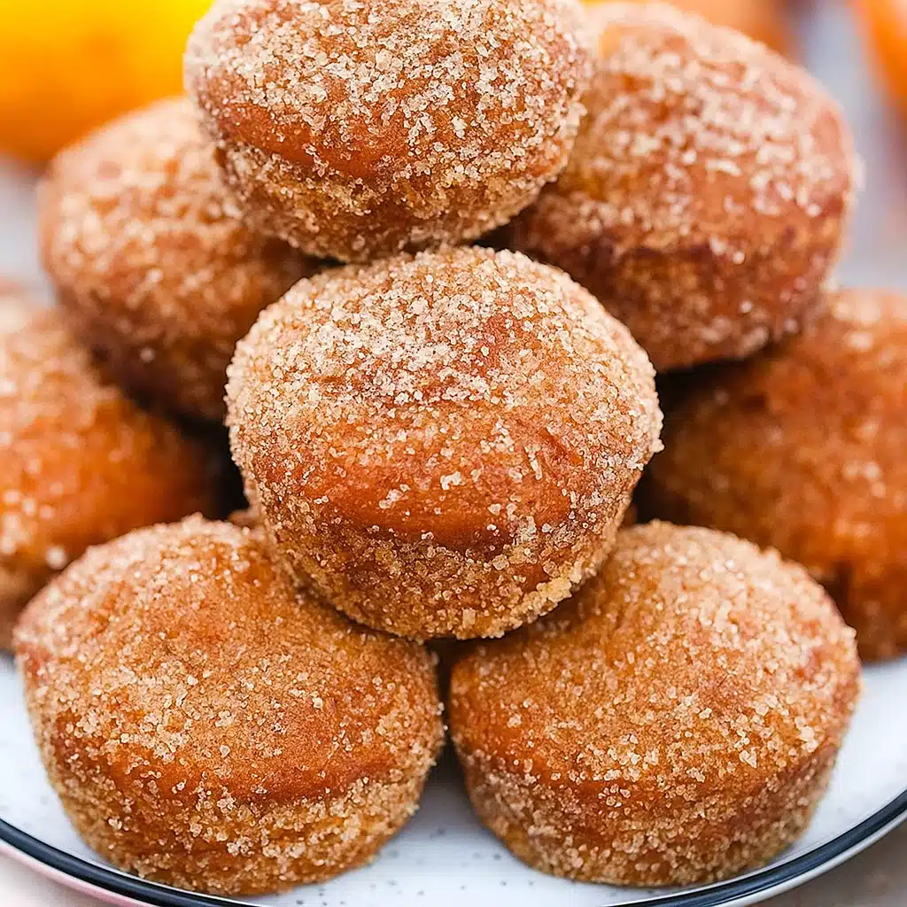 Golden-brown donut pumpkin muffins coated in cinnamon sugar, arranged on a rustic wooden board with fall leaves in the background
