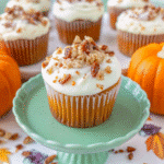 Golden pumpkin pecan cupcakes topped with swirled cinnamon cream cheese frosting and chopped pecans on a rustic wooden table with fall leaves