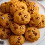 Soft, chewy pumpkin chocolate chip cookies with golden edges and melted chocolate chips, arranged on a cooling rack with fall decorations in the background.