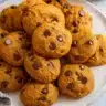 Soft, chewy pumpkin chocolate chip cookies with golden edges and melted chocolate chips, arranged on a cooling rack with fall decorations in the background.