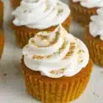 Pumpkin pie cupcakes with whipped cream on top, sitting on a wooden board with some fall leaves around them