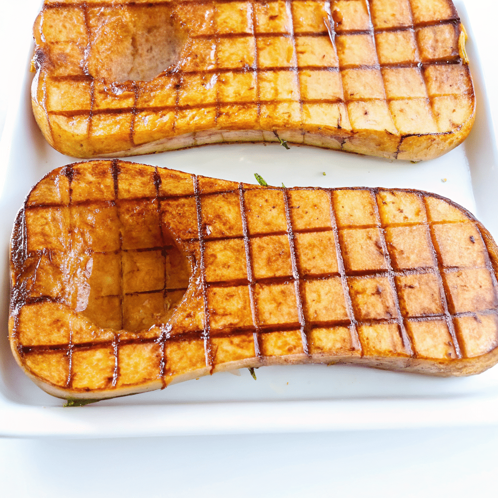 Golden, caramelized cubes of honey roasted butternut squash on a white serving platter, garnished with fresh herbs