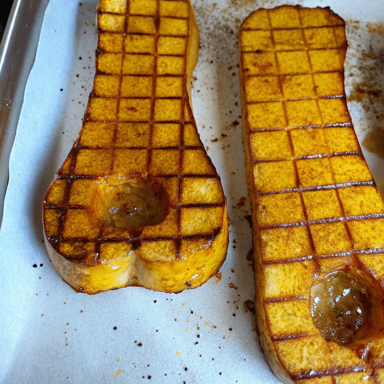 Golden, caramelized cubes of honey roasted butternut squash on a white serving platter, garnished with fresh herbs