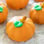 Pumpkin Oreo Balls treats resembling mini pumpkins with green M&M stems on white parchment paper