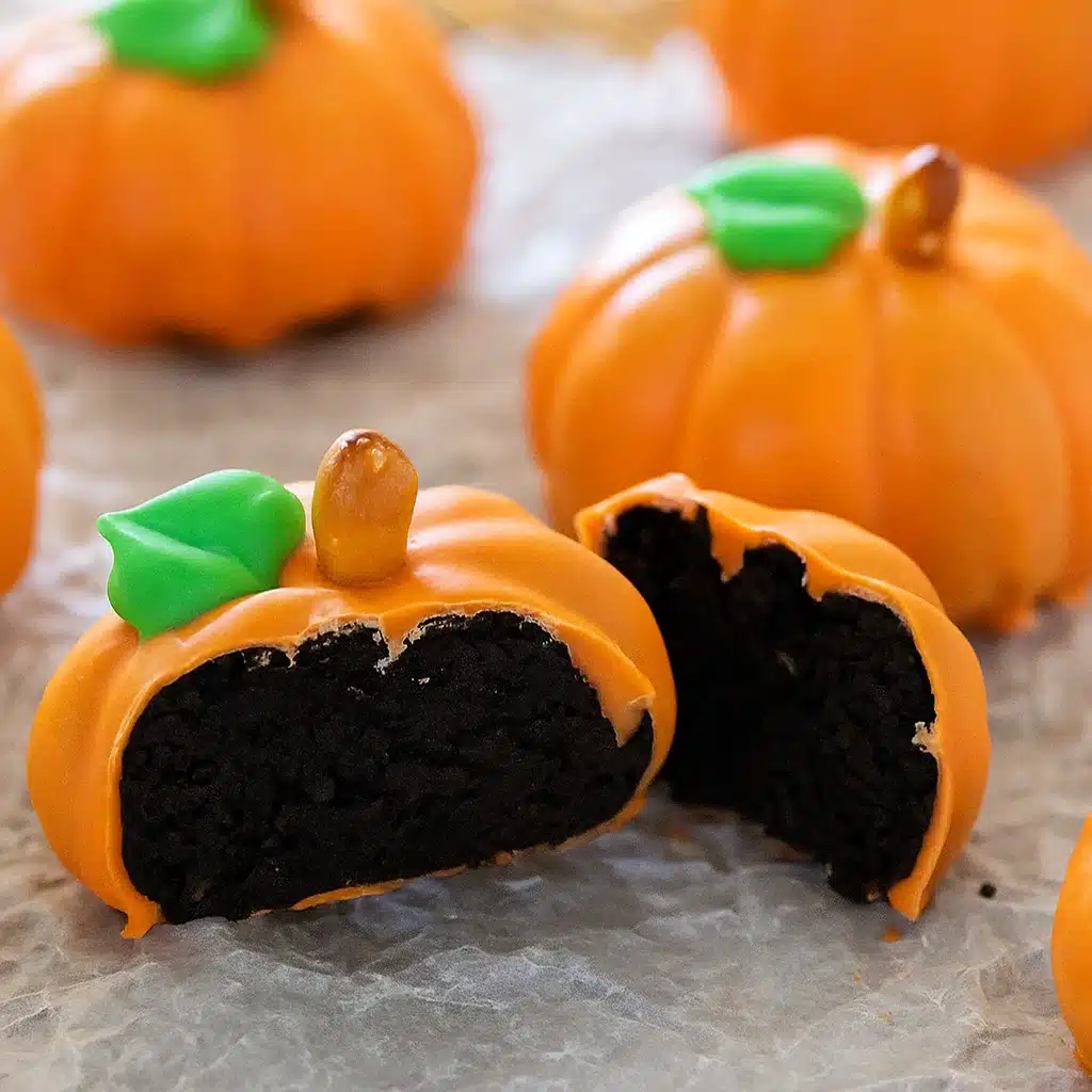 Orange-coated round treats resembling mini pumpkins with green M&M stems on white parchment paper