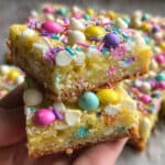Easter cake mix cookie bars cut into squares on a white platter, topped with pastel icing drizzle and colorful spring sprinkles