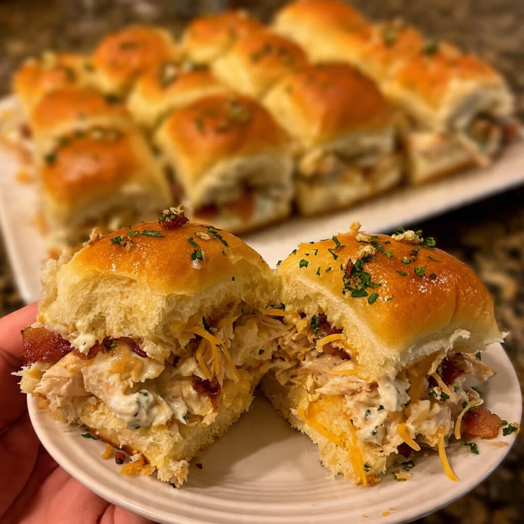 chicken bacon ranch sliders in a baking dish, showing melted cheddar cheese and herb butter topping on Hawaiian rolls